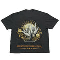 A black short-sleeve t-shirt laid flat against a light gray background, showing the back side with a graphic print of two hands making the shaka sign, surrounded by yellow flowers and rays, with the text 'MY HANDS ARE MY VOICE AND MY VOICE IS BEAUTIFUL.'.