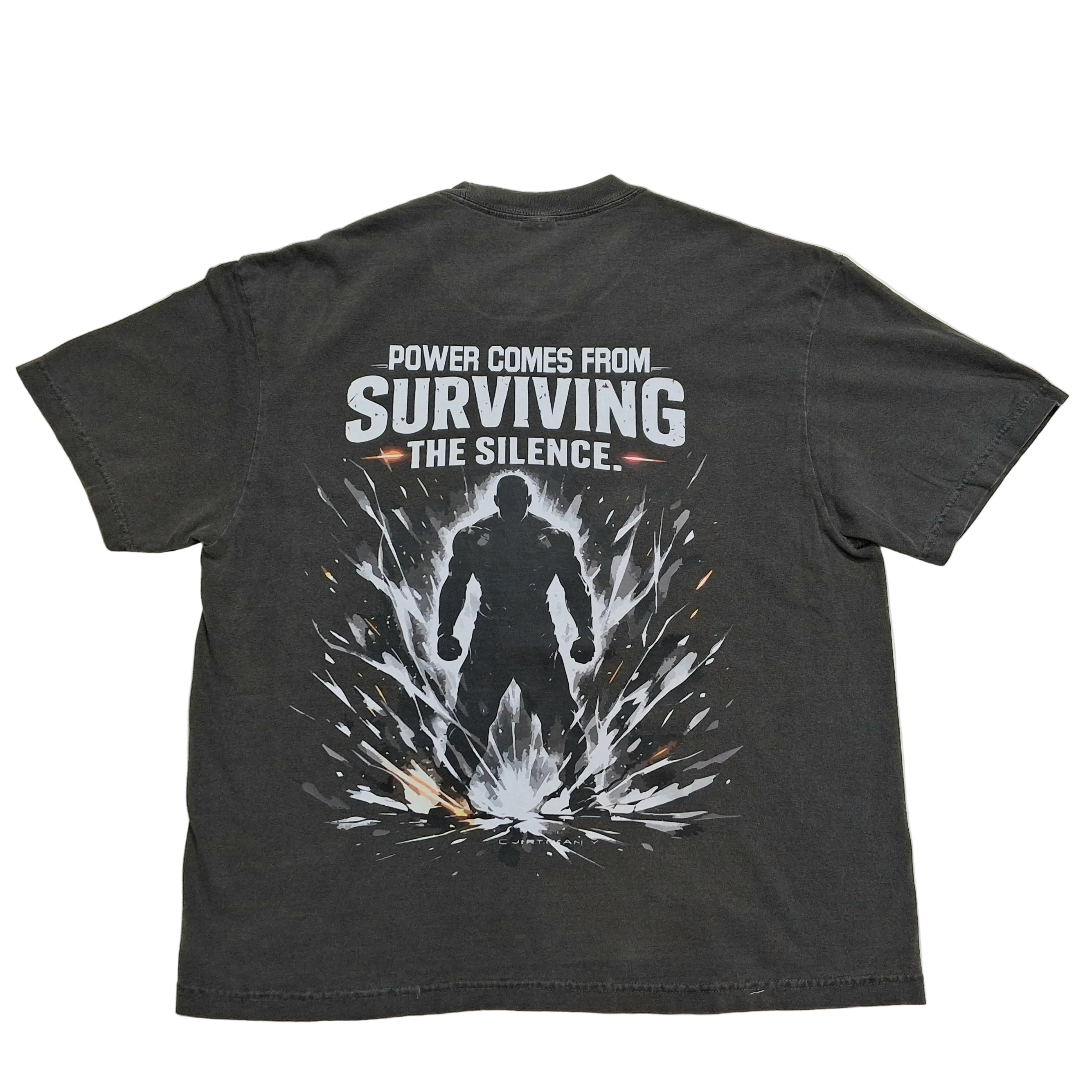 A dark gray graphic t-shirt laid flat on a light gray background, showing the back side with a white and black design that reads 'POWER COMES FROM SURVIVING THE SILENCE.'.