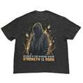 A dark charcoal gray graphic t-shirt laid flat on a light gray background. The Back of the shirt features a graphic of a hooded figure surrounded by orange and yellow flames, with the text 'SILENCE IS THE SHADOW WHERE STRENGTH IS BORN' printed below in white and orange.