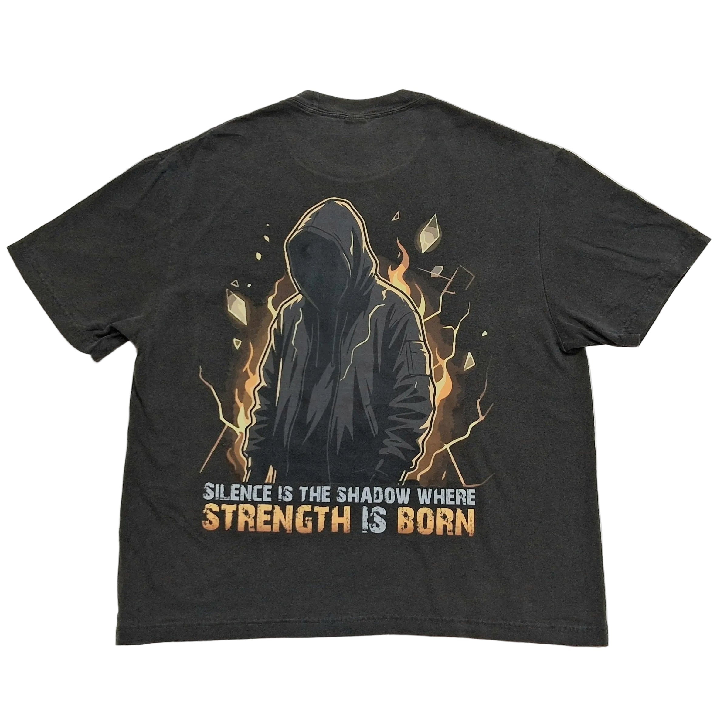A dark charcoal gray graphic t-shirt laid flat on a light gray background. The Back of the shirt features a graphic of a hooded figure surrounded by orange and yellow flames, with the text 'SILENCE IS THE SHADOW WHERE STRENGTH IS BORN' printed below in white and orange.