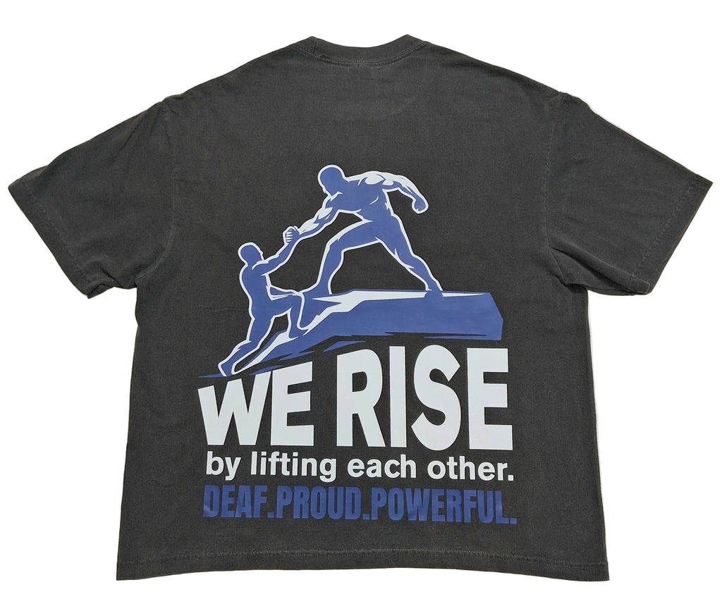A dark charcoal gray t-shirt showing the back side, which features a graphic of two blue figures lifting each other up. Below the graphic, the text reads 'WE RISE by lifting each other.